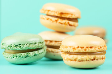 Fototapeta premium a group of fresh macarons in mint green and creamy beige colors scattered on a turquoise blue surface. the macro shot emphasizes the crunchy texture of the shells and rich caramel filling