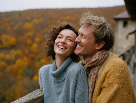 A happy couple wearing warm sweaters relaxes at their countryside retreat, taking in the stunning view of yellow and red autumn leaves. Peaceful, loving lifestyle.