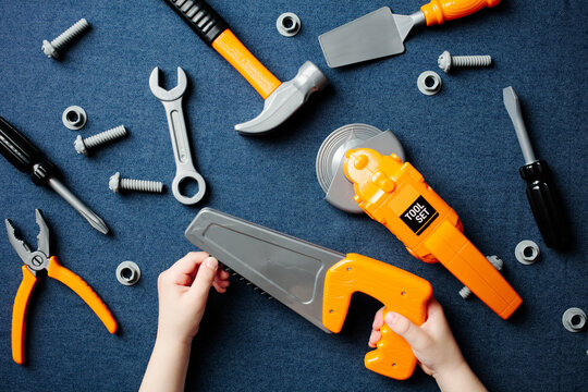 Child's hands holding toy saw, construction tool set play on denim.
