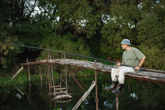 Fisherman with fishing rod on a footbridge near the lake at summer