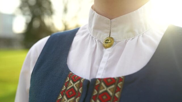 Traditional Latvian folk costume detail featuring a decorative button and embroidered patterns in a natural outdoor setting