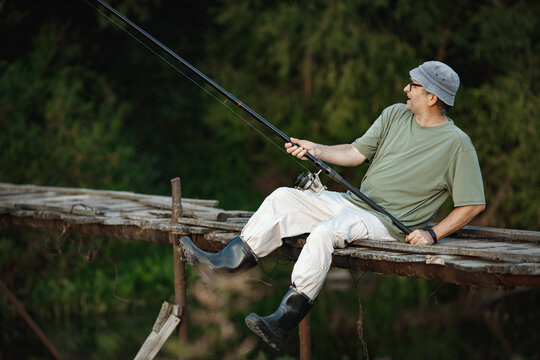 Fisherman with fishing rod on a footbridge near the lake at summer