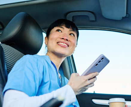 Female nurse sitting in car, using a smartphone, going home from work. Female doctor driving car to work, on-call duty.