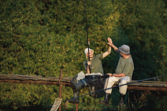 Two fishermen with fishing rods on a footbridge near the lake at summer