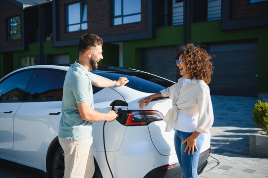 Happy couple charging electric car at home, embracing green energy and sustainable lifestyle