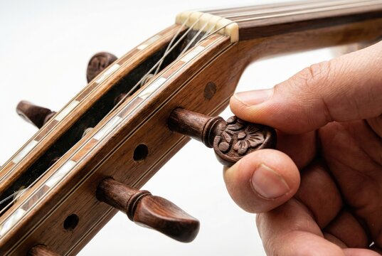 Musician hand turning the carved wooden tuning peg of a traditional stringed instrument