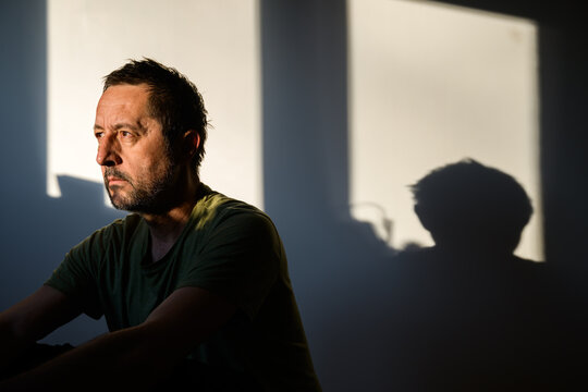 Close-up of thoughtful adult male in side light with glowing outline and moody shadows, expressive portrait conveying contemplation and inner strength.