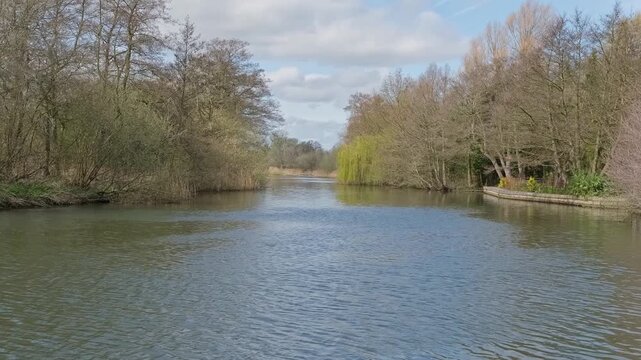 A peaceful, sunlit view down the River Bure in the Norfolk Broads, filmed from Belaugh Staithe. Trees line the riverbank capturing the quiet charm of a perfect summer day on the Norfolk Broads. 
