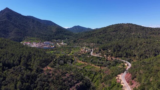 Panoramic view of Sierra Espadan natural park with the small village of Ain surrounded by dense pine forests, winding mountain road and terraced fields in Castellon, Spain