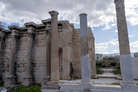 Close-up view of the majestic Corinthian columns and the surviving stone wall of Hadrian's Library under a cloudy sky in Athens, Greece.