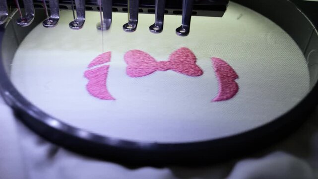 Machine embroidery of ribbons on white textile with pink thread.