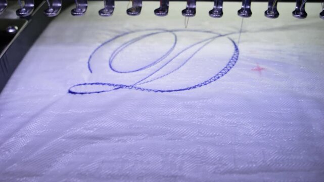 Machine embroidery of the letter "D" on white fabric with blue thread. Selective focus close-up
