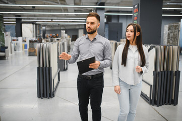 Salesman advising female customer choosing tiles in store