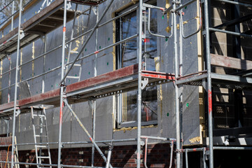 Naklejka premium Scaffold structure beside unfinished building wall with insulation panels and windows, highlighting facade installation and retrofit project