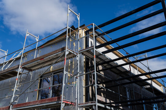 Scaffolding and steel roof beams above insulated building facade during renovation, showing retrofit work and exterior construction progress