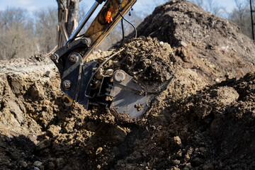 Fototapeta premium Excavator bucket digging through dense soil at construction site, showing earthmoving work, trench excavation and heavy equipment action