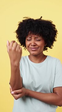 Young woman suffering from elbow pain on yellow background