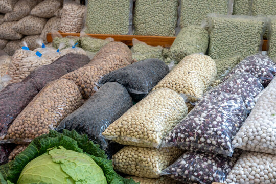 A variety of dried beans, including traditional Asturian "fabes," lentils, and black beans in plastic sacks displayed at an outdoor local market
