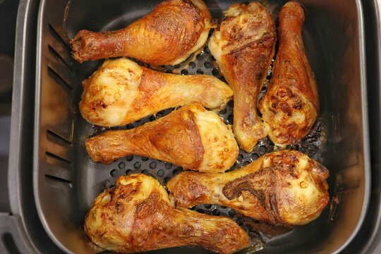 Golden-brown roasted chicken drumsticks inside an air fryer basket ready to be served. Concept of quick healthy cooking.
