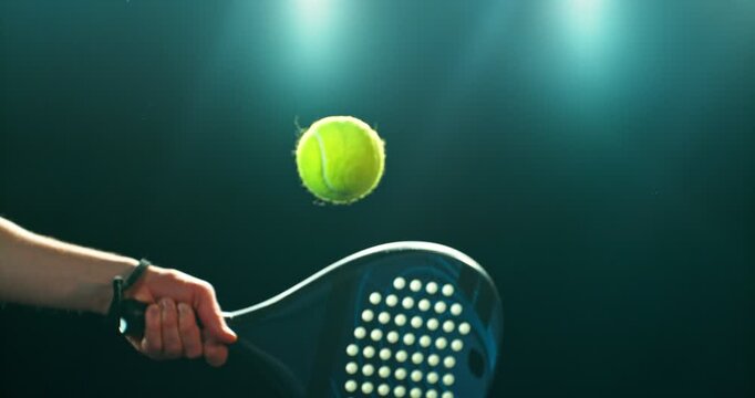 Super slow motion close-up of a hand holding a padel racket as a yellow ball hits the surface, filmed at 1000 fps. Dramatic studio lighting highlights the impact, motion of the racket and ball.