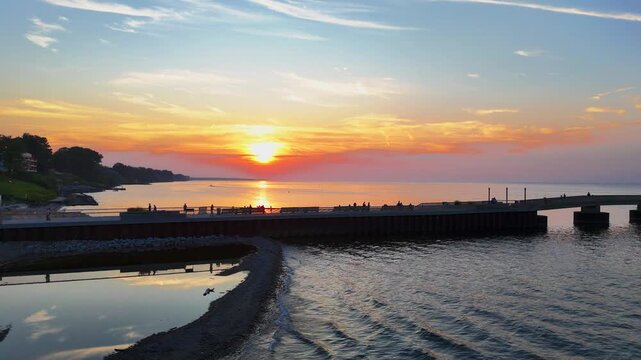 Parallel Drone Along Pier at Sunset Fishermen/ 4K parallel drone flight along pier at sunset with fishermen and small waves. Bright sun flare, coastal evening scenery.

