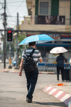 Man walking through city street holding umbrella, health safety and protection from heatstroke during heatwave, male hiding from sun under umbrella while passing by crossroad on hot summer day.
