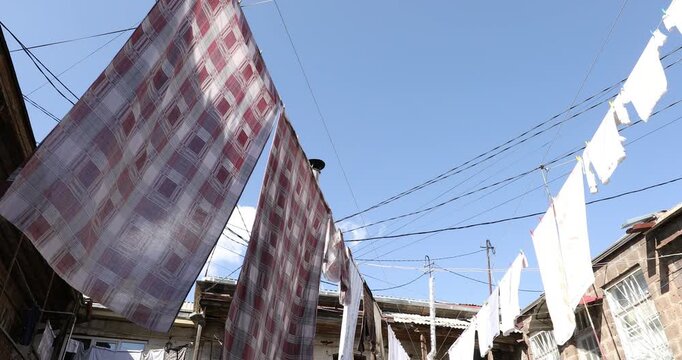 A slow panning shot reveals colorful laundry hanging on a clothesline to dry in the bright sunlight, strung across a courtyard in front of an old stone building.