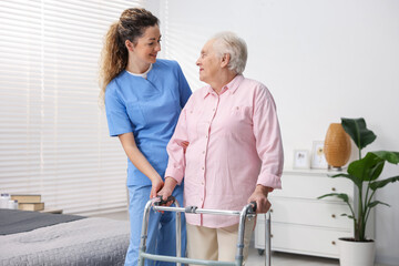 Fototapeta premium Care worker helping senior woman with walker indoors
