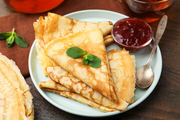 Tasty crepes with jam and mint leaves served on wooden table, closeup © New Africa