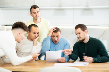 Fototapeta premium Friends reading financial documents and trying to solve problems together while sitting at table in their home kitchen