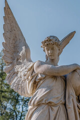 Fototapeta premium Statue of angel with wings against blue sky, symbol of protection, peace, memory and spirituality.