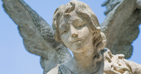 Fototapeta premium Close-up of stone angel statue with wings against blue sky, memorial sculpture symbolizing peace, spirituality, grief and eternity.