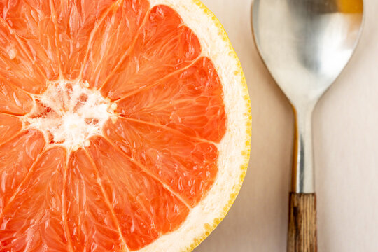 Half of a grapefruit with a spoon on a light surface 