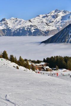 View from Courchevel ski resort by winter with chalets and skiers on the slopes and under cloud in front of Mont Blanc, French alps