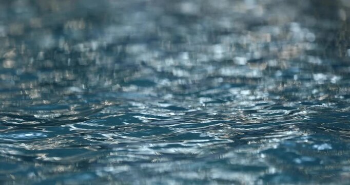 Close up of vibrant blue swimming pool water with gentle ripples. Bright sunlight reflects on the moving liquid surface, creating a truly relaxing, calming abstract background texture pattern.

