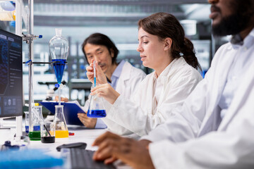 Fototapeta premium Team of chemists working together, using pipette to dispense reagent into test tube at laboratory bench. Teamworking research facility colleagues do pipetting procedure with dropper