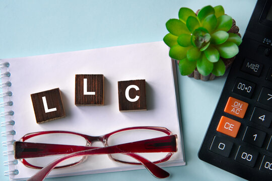 LLC - acronym on wooden cubes with a calculator and glasses in the background