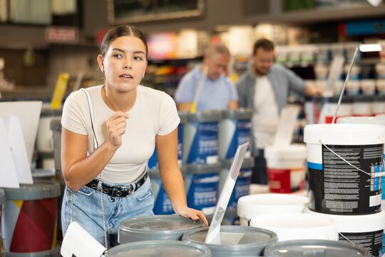 Woman buys tin with paint in paintwork material department of construction store for carrying out internal finishing work on object