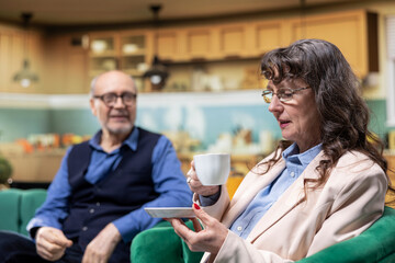 Fototapeta premium Retired senior couple, relaxing together, coffee in living room, peaceful home, retirement lifestyle. Husband and wife, comfort and companionship, longevity, independence, and domestic life.