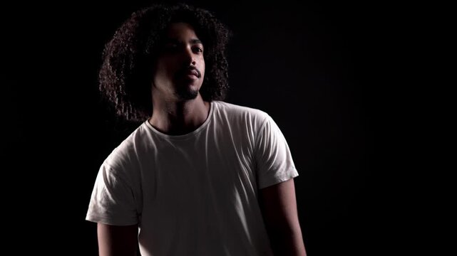 Confident young man with afro hair dancing and moving rhythmically against a dark background