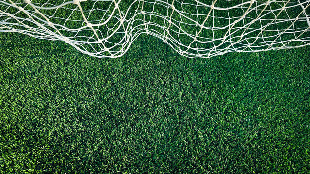 Overhead banner sized view of a white soccer goal net on vibrant, newly installed synthetic green turf. A crisp, high-contrast background for sports and athletic themes.