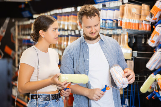 Married couple choose paint brush and paint roller together for their home renovation at a hardware store