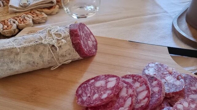 View food in Easter time in Italy, with Sliced cured salami on wooden board with whole sausage wrapped in lace, rustic food