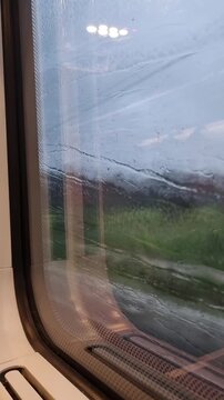 Train travel with rainy view through a train window with blurred countryside and water droplets on glass. Motion-blurred rural scenery seen through a wet window