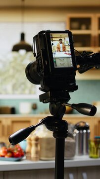 Behind the scenes with black woman filming a new recipe in home kitchen, using camera on tripod for food vlog content. Young solo chef recording cooking process and preparation at counter.