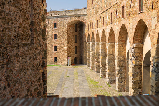Interior view of the courtyard of the Medieval Fortress with Stone Arches of Priamar in Savona, Liguria, Italy. Close-up of an ancient fortified courtyard with a rustic stone arched gallery, medieval