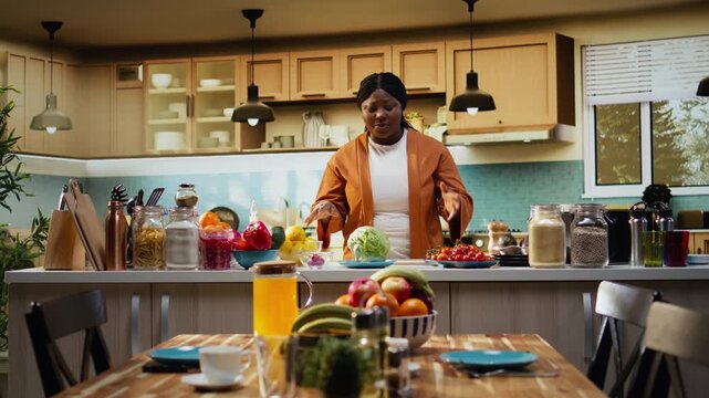 Black woman chef recording a cooking tutorial video at the kitchen counter under natural light. Food influencer shows meal prep and salad preparation steps for her vlog channel.