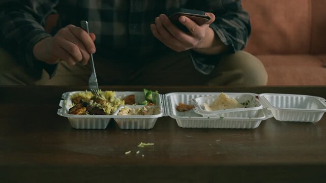 Man scrolling his phone on the sofa while eating takeaway