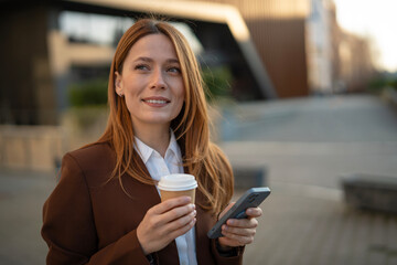 Professional woman holding coffee and phone walking city