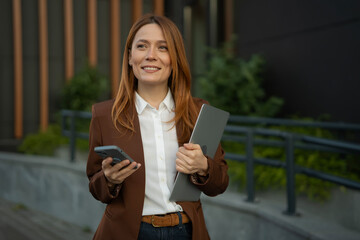 Businesswoman walking in city holding phone and laptop